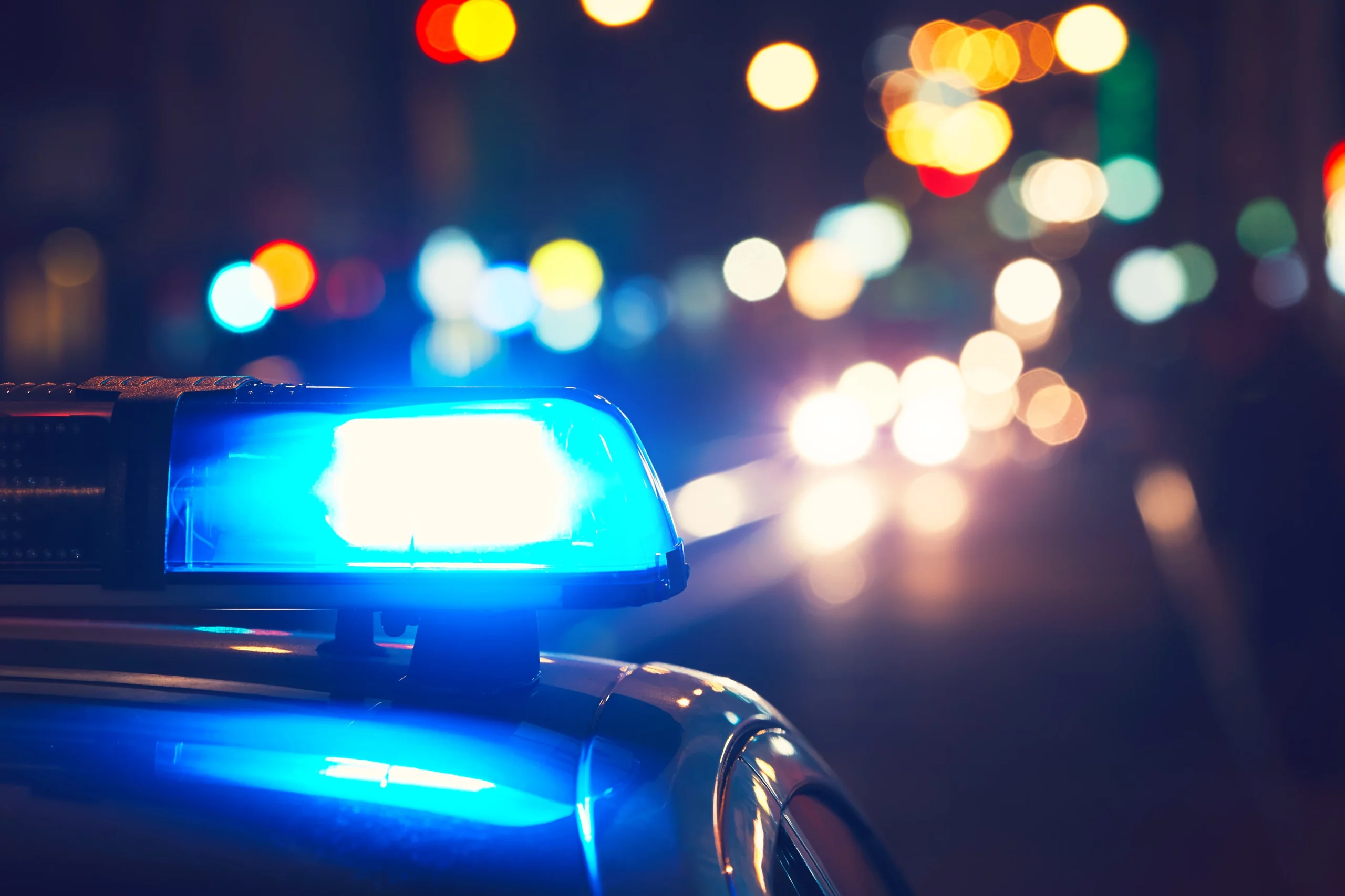 Close-up of a police car’s blue siren flashing at night with city lights, illustrating law enforcement responding to reckless driving or DUI incidents in Georgia and the legal consequences of each offense.