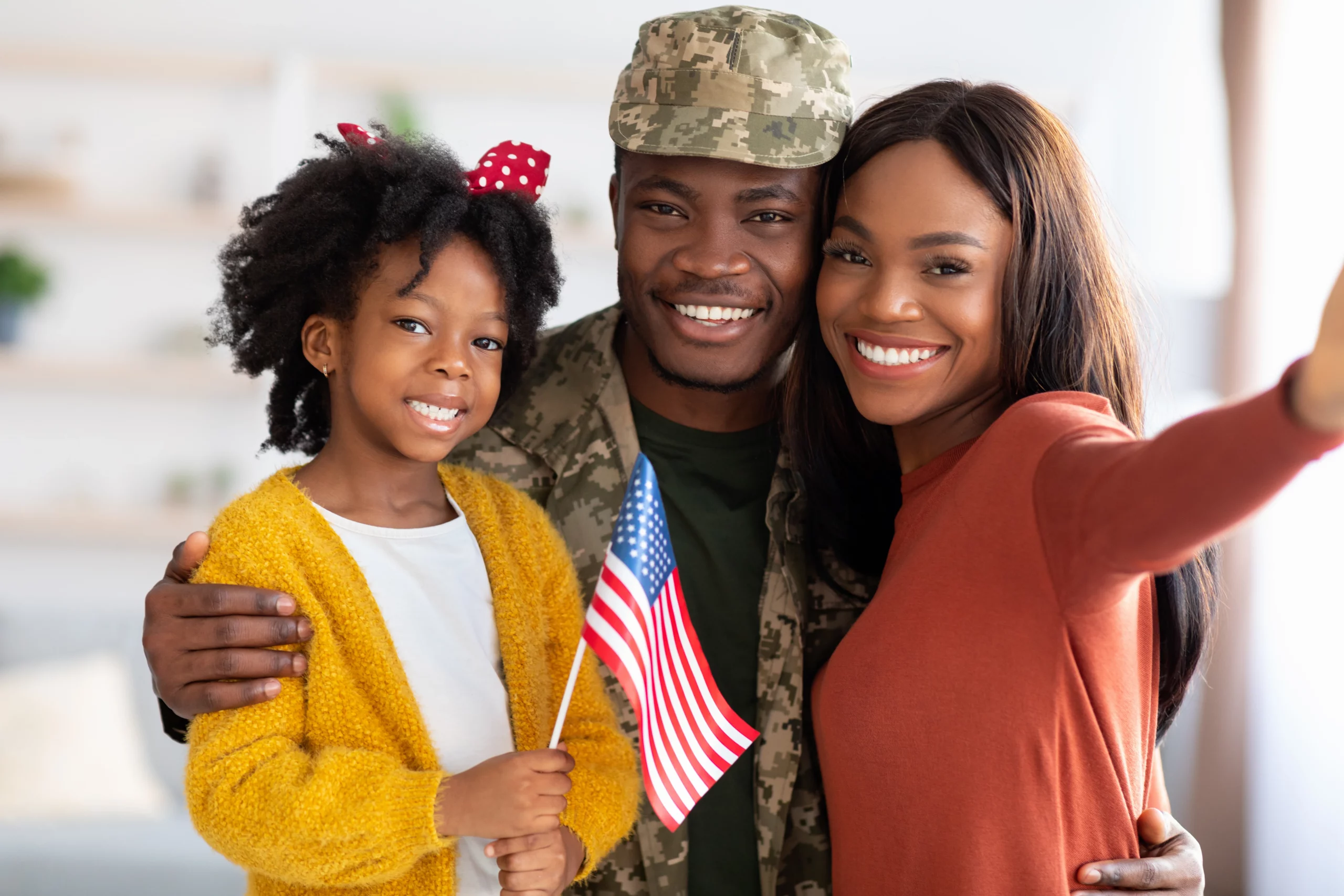 Smiling military family with a service member in uniform and a child holding an American flag, representing military parole in place that helps eligible family members of U.S. service members remain in the country legally.